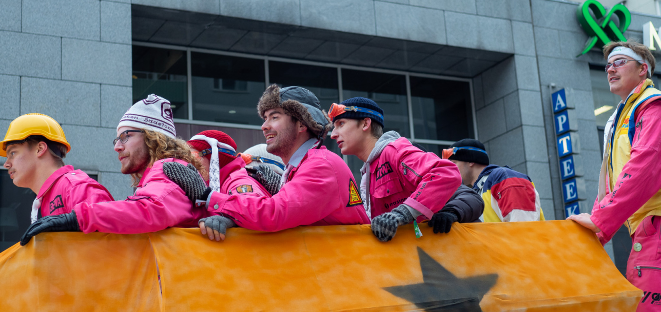 Viisi opiskelijaa kirkkaan pinkeissä haalareissa katsoo alas kisamäkeen odottaen vuoroaan.