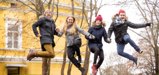 Neljä nuorta aikuista hyppää ilmaan syksyisessä maisemassa.