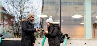 Kaksi opiskelijaa päivittämässä somea kampuksella kirjaston edessä.