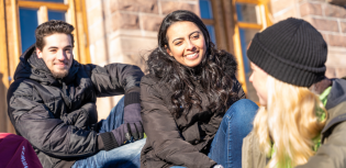 Kolme opiskelijaa istun ulkoportailla.