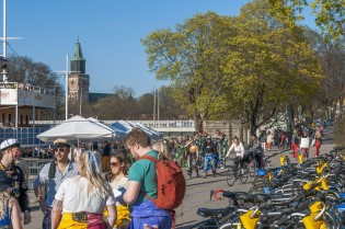 Opiskelijoita Turun jokirannassa keväällä, taustalla Tuomiokirkko ja jokilaivat.