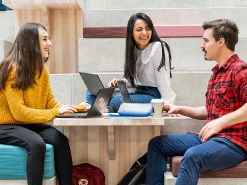 Kolme opiskelijaa kannettavien tietokoneiden kanssa korkeakoulun tiloissa.